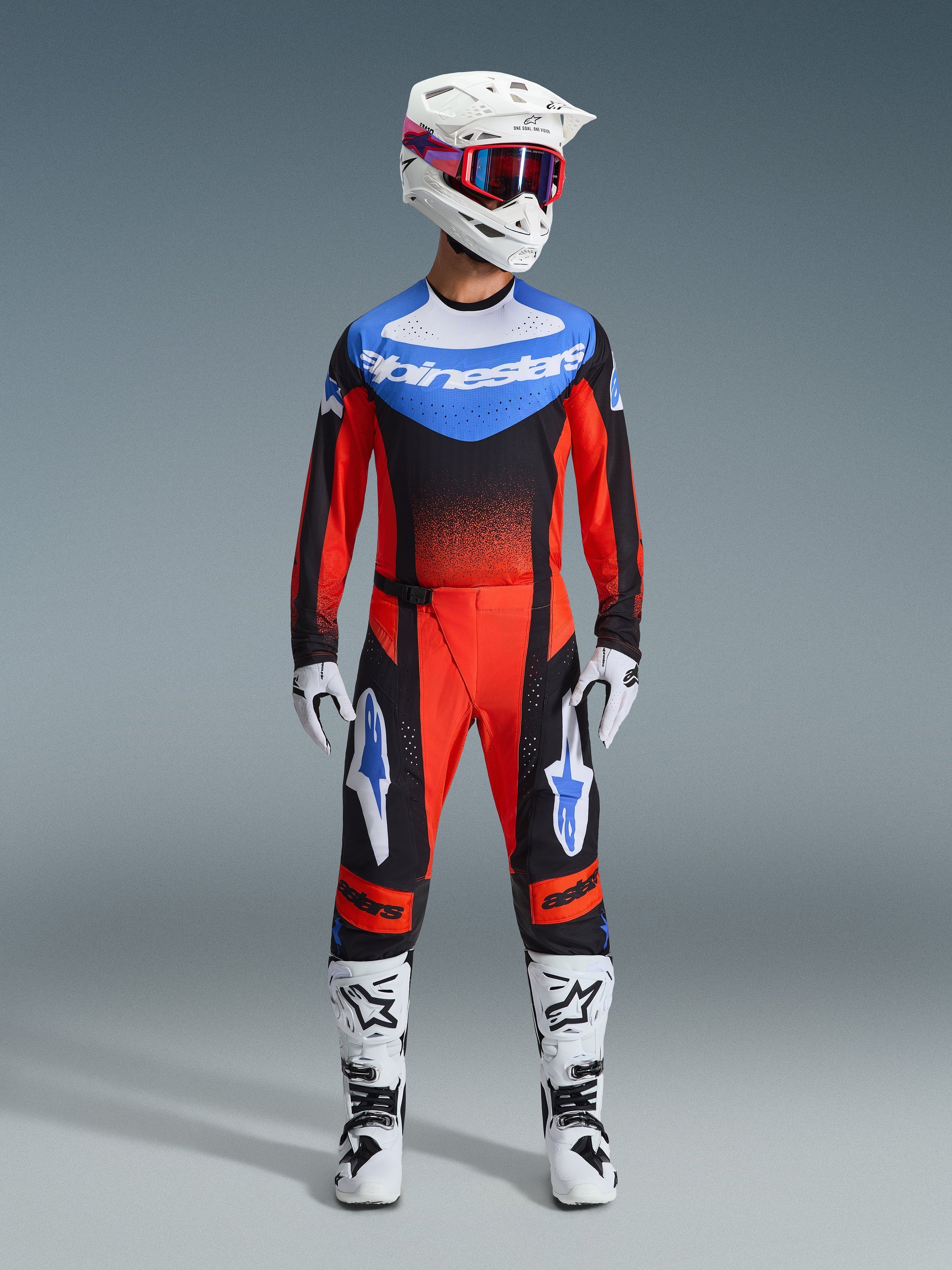 Piloto de motocross con equipamiento completo de carreras, jersey naranja y negro con detalles azules, pantalones Techstar Knif en naranja, negro y azul UCLA, casco blanco con gafas rojas, botas blancas y negras, guantes blancos y negros, conjunto coordinado para competición off-road