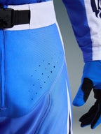 Alpinestars Techstar Knif Pants 2026, azul UCLA y blanco, primer plano de la zona de la cadera con perforaciones láser para ventilación, cierre de cintura con hebilla magnética SX2 y guantes de motocross a juego