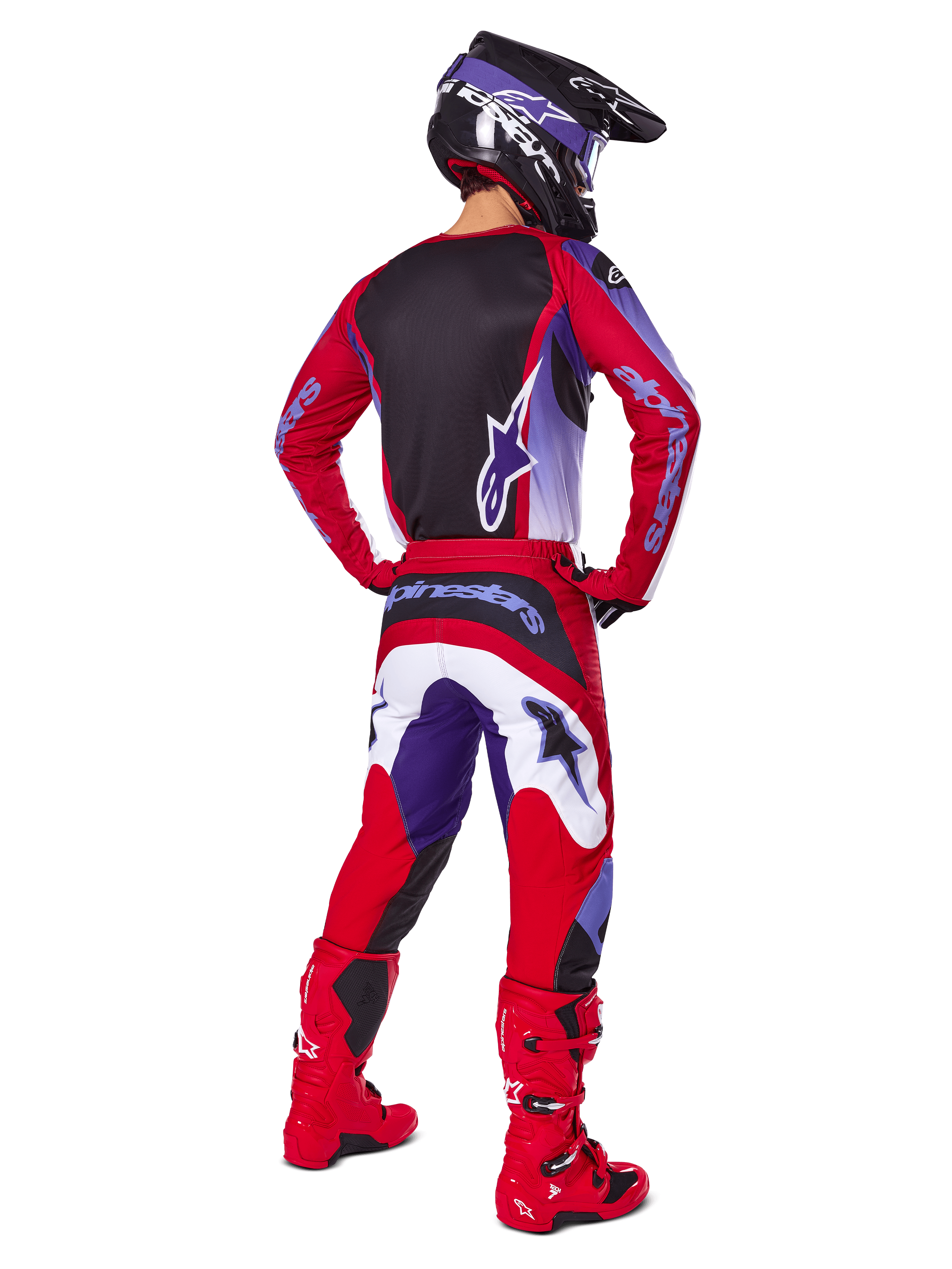 Piloto de motocross desde atrás vistiendo pantalones Alpinestars 2025 Fluid Wurx, púrpura y rojo brillante con detalles en blanco y negro, jersey a juego, casco negro y botas rojas, conjunto coordinado para carreras off-road