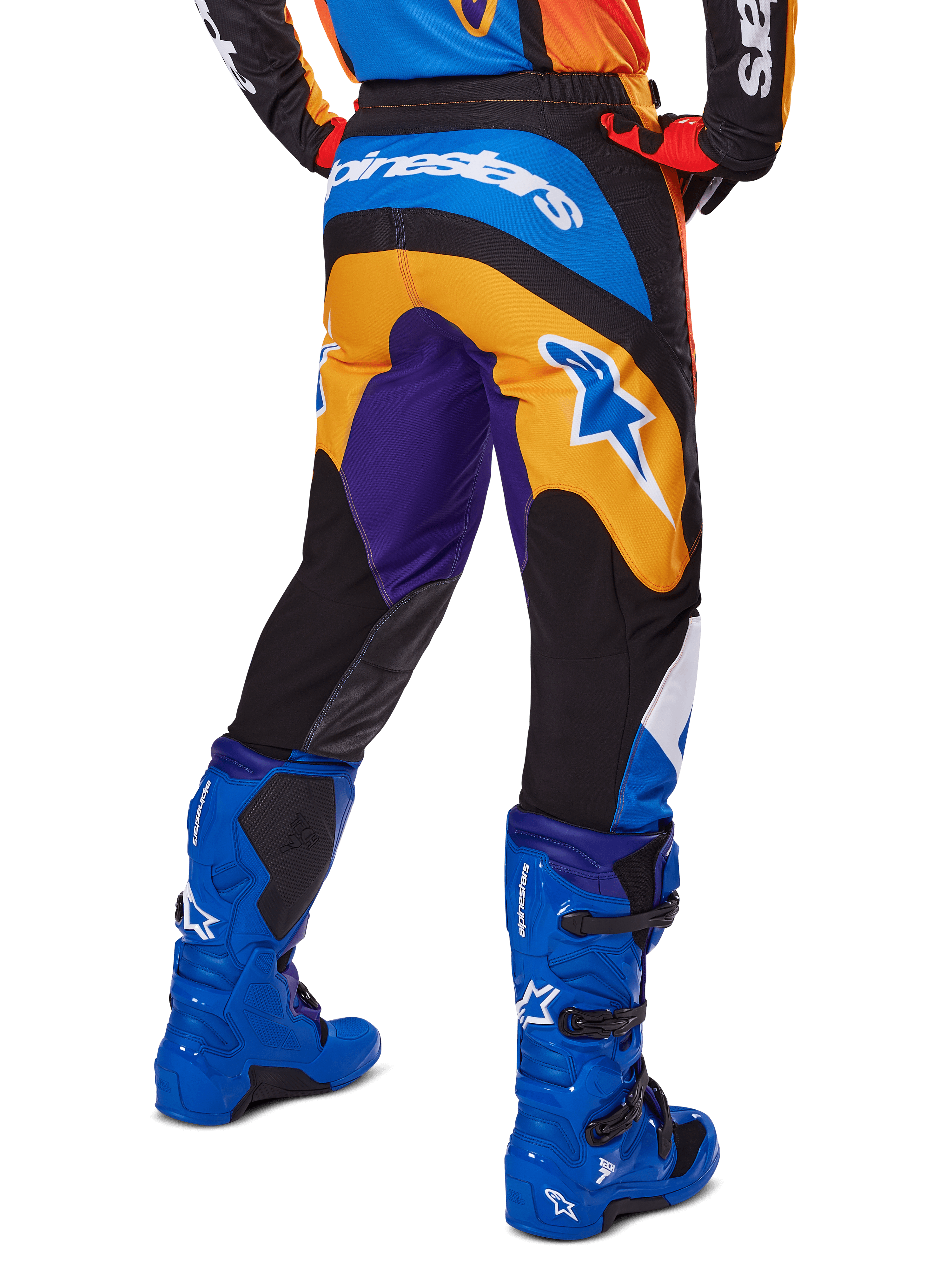 Alpinestars 2025 Fluid Wurx Pants, pantalones de motocross, multicolor con naranja, morado y azul, vista trasera que muestra el logotipo blanco de Alpinestars en la parte posterior, combinados con botas de motocross azules, ajuste atlético para carreras todoterreno