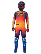 Pantalones Alpinestars Fluid Wurx 2025, pantalones de motocross, degradado multicolor en naranja, amarillo y púrpura, usados con el jersey a juego, casco negro con gafas azules, guantes rojos y negros, y botas azules, equipo de motocross coordinado.