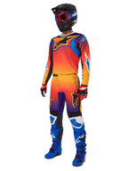 Piloto de motocross con equipamiento completo de carreras, pantalones Alpinestars 2025 Fluid Wurx y jersey a juego en un degradado multicolor naranja, rojo y morado, casco negro con gafas rojas, botas azules y negras, y guantes rojos y negros, conjunto coordinado para carreras todoterreno