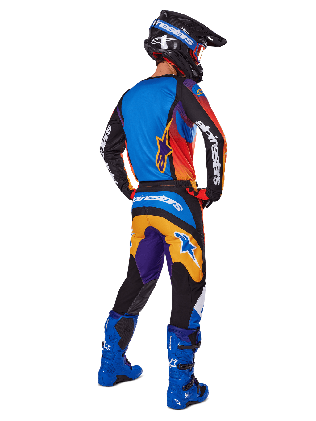 Piloto de motocross visto desde atrás con pantalones Alpinestars Fluid Wurx 2025, diseño multicolor con detalles en azul, naranja, amarillo y púrpura, combinados con un jersey a juego, botas azul brillante y casco negro, equipamiento completo de competición off-road