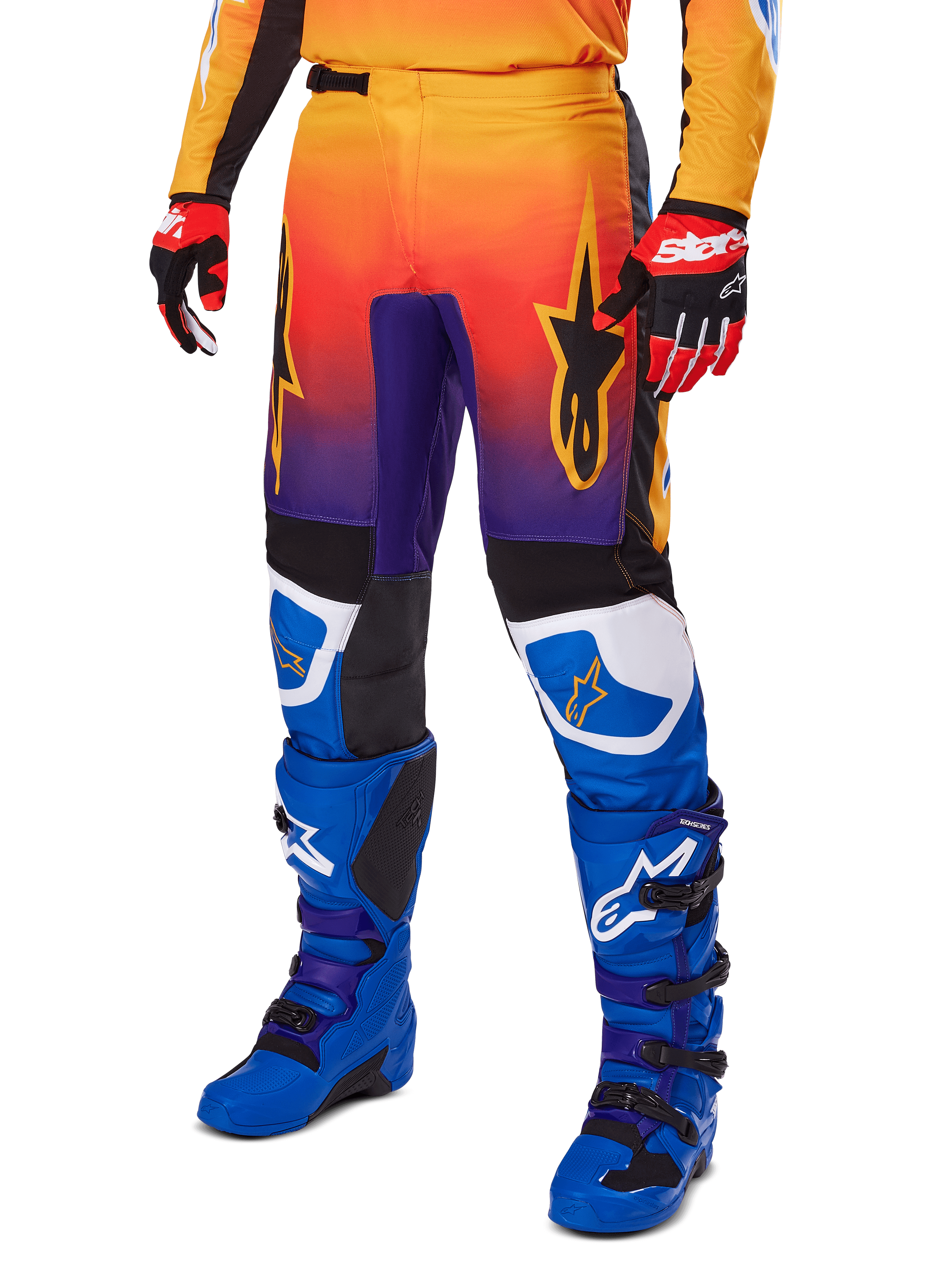 Alpinestars 2025 Fluid Wurx Pants, pantalones de motocross, degradado multicolor en naranja, rojo y púrpura con paneles negros y azules, usados con botas azules y guantes rojos, con gráficos del logo de estrella y detalles blancos en las rodillas, equipamiento de alto rendimiento para carreras todoterreno