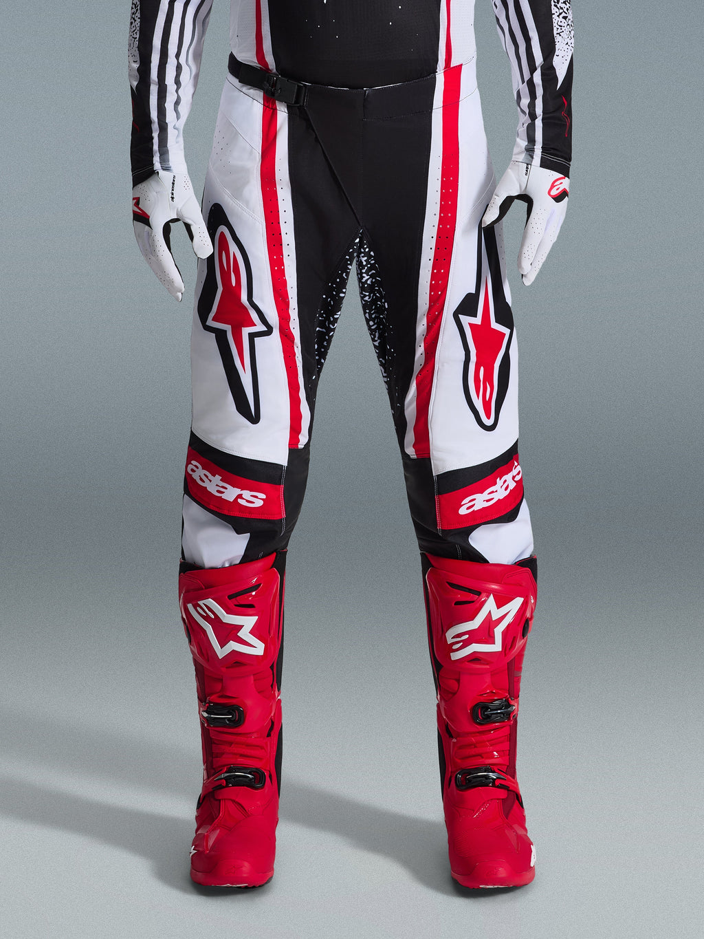 Alpinestars 2026 Techstar Nomur Pants, pantalones de motocross, negro, blanco y rojo, combinados con botas rojas a juego y guantes blancos, con logotipos rojos llamativos en los muslos y marca 'astars' en las rodillas, diseño de competición de paneles múltiples para rendimiento todoterreno
