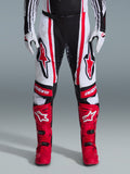 Alpinestars 2026 Techstar Nomur Pants, pantalones de motocross, negro, blanco y rojo, combinados con botas rojas a juego y guantes blancos, con logotipos rojos llamativos en los muslos y marca 'astars' en las rodillas, diseño de competición de paneles múltiples para rendimiento todoterreno