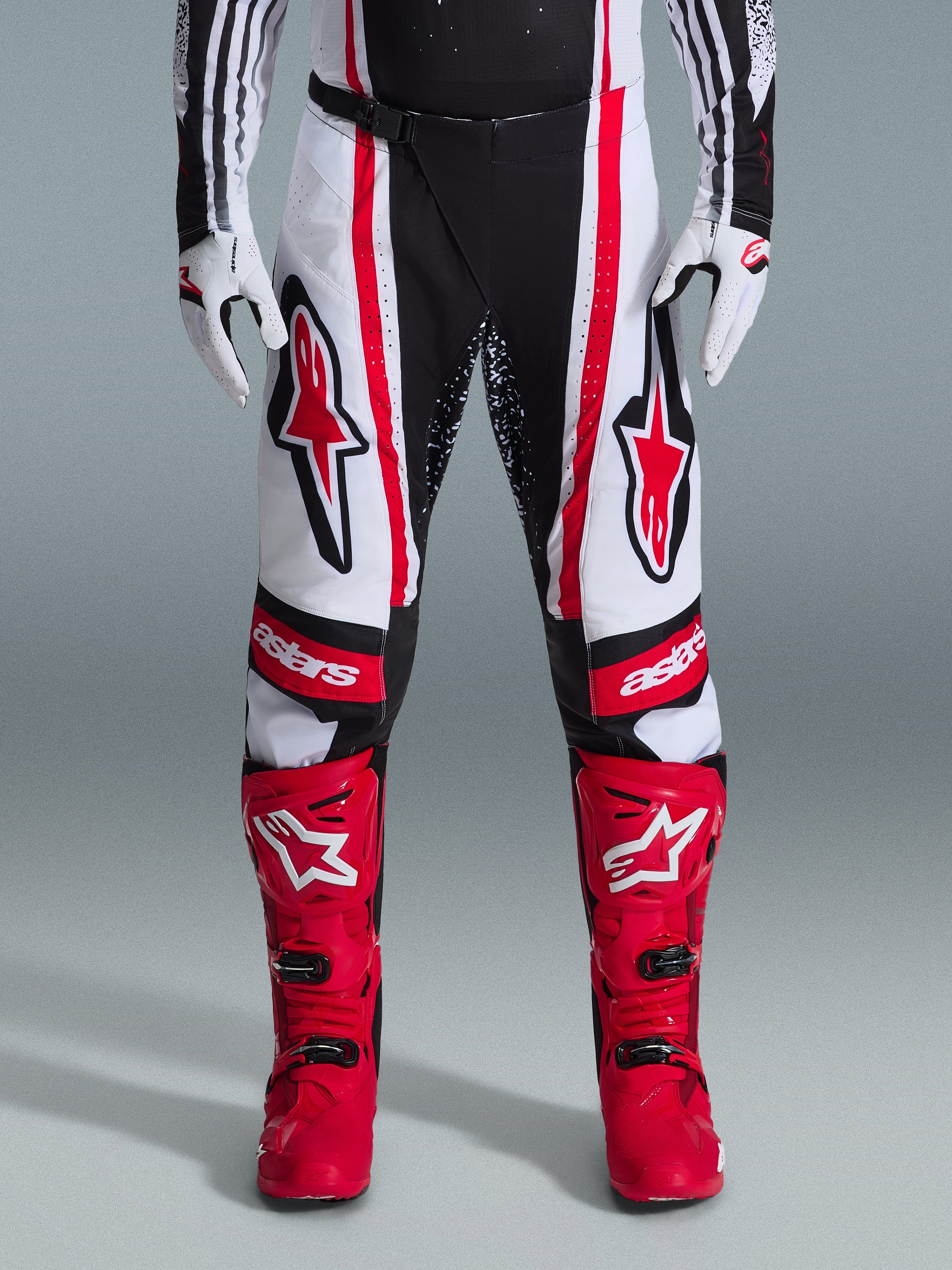 Alpinestars 2026 Techstar Nomur Pants, pantalones de motocross, negro, blanco y rojo, combinados con botas rojas a juego y guantes blancos, con logotipos rojos llamativos en los muslos y marca 'astars' en las rodillas, diseño de competición de paneles múltiples para rendimiento todoterreno