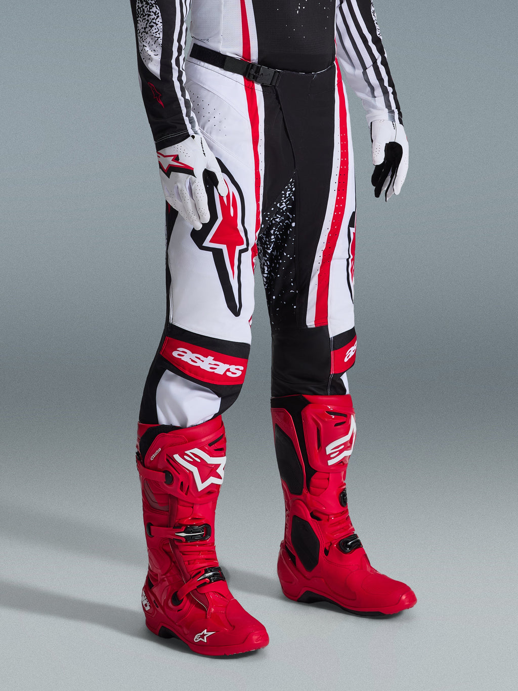Alpinestars 2026 Techstar Nomur Pants, pantalones de motocross, negro, blanco y rojo, combinados con botas de carreras de color rojo vibrante y guantes blancos, con rayas verticales llamativas, un gran logotipo de estrella roja en el muslo y paneles reforzados en las rodillas para rendimiento todoterreno.