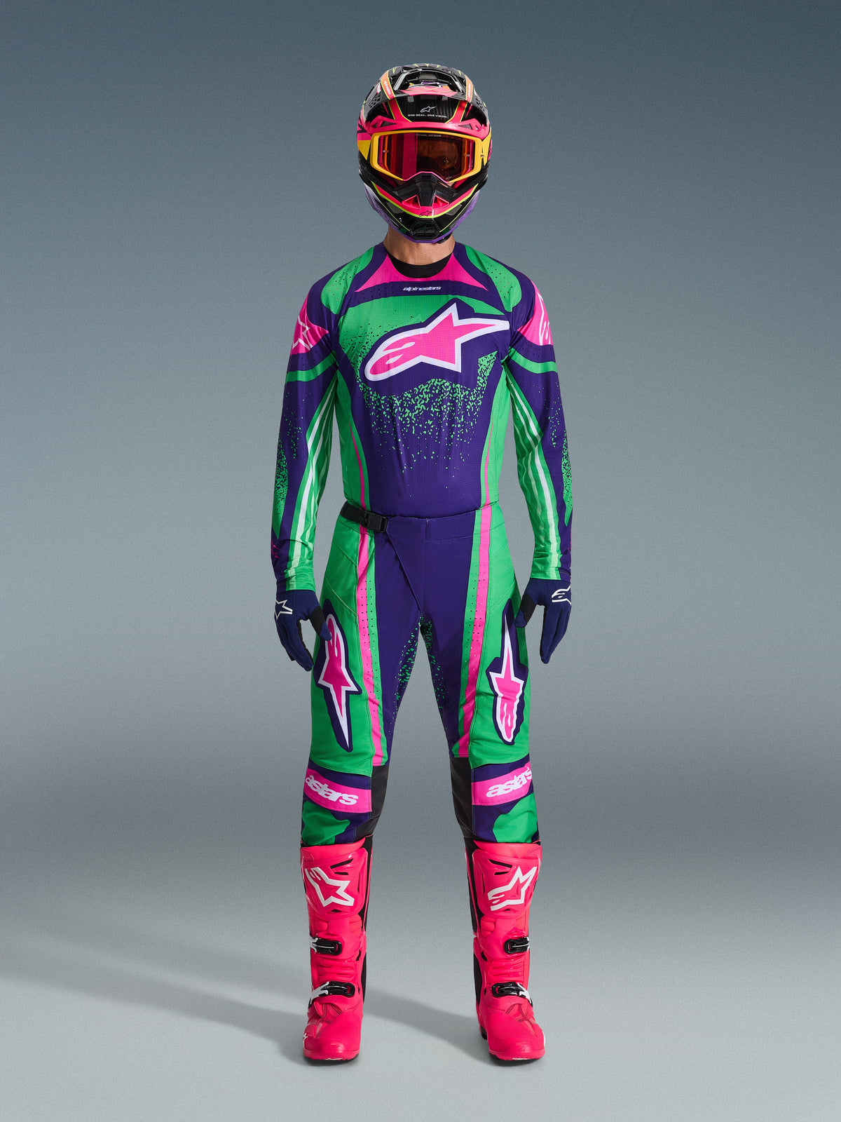 Alpinestars 2026 Techstar Nomur Gear Set, conjunto de motocross, verde, morado y rosa vibrante, gran logotipo de estrella en el pecho y los muslos, casco negro con detalles en rosa y amarillo, botas rosa brillante, diseño deportivo profesional
