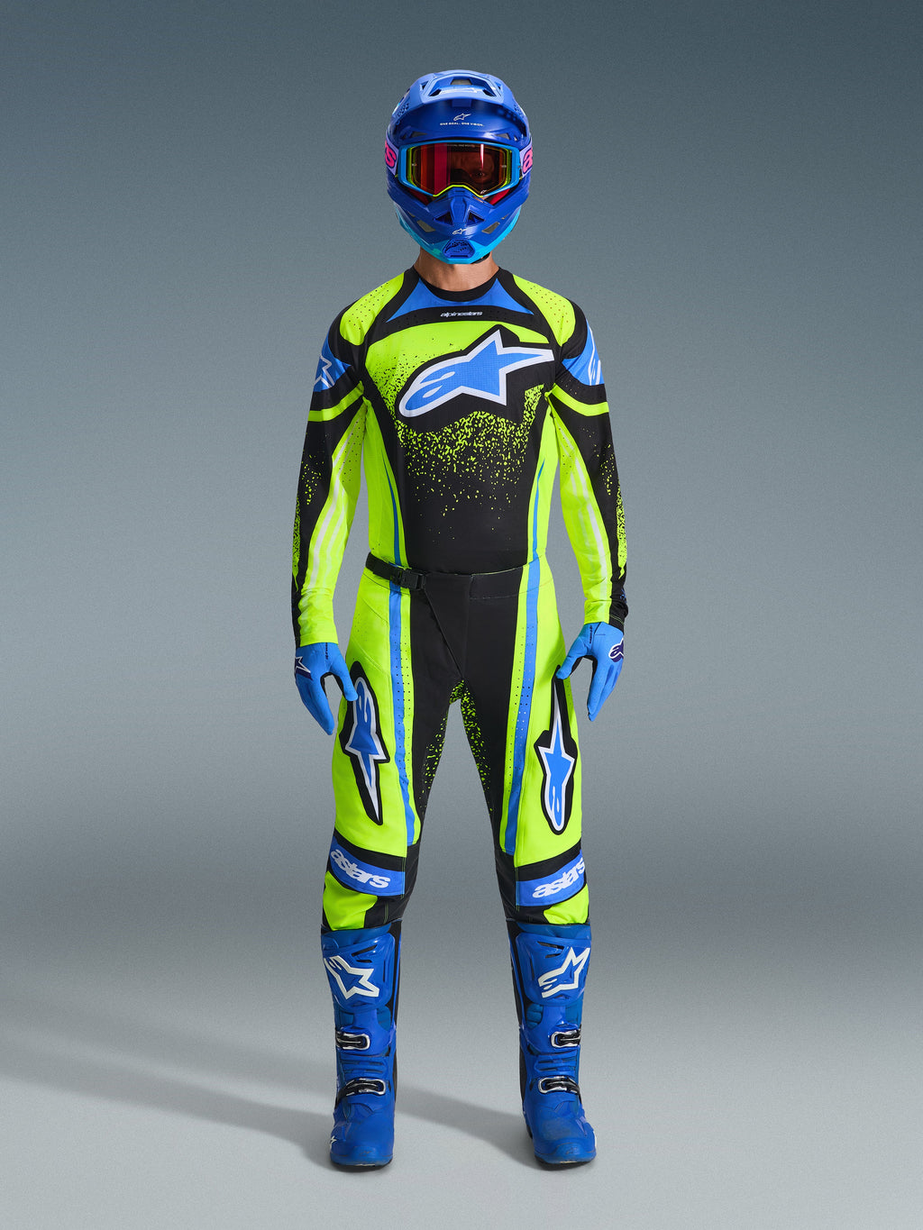 Motocross rider wearing the Alpinestars 2026 Techstar Nomur Gear Set, Fluorescent yellow and black jersey with a large blue star logo, matching yellow and black pants, blue helmet with goggles, blue gloves, and blue boots, complete professional motocross outfit for off-road racing