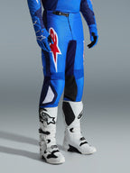 Alpinestars 2026 Fluid Grid Pants, pantalones de motocross, azul y rojo, usados con botas de motocross blancas y guantes azules, con un gran logotipo de estrella roja en el muslo y paneles internos negros en las rodillas, diseñados para conducción off-road