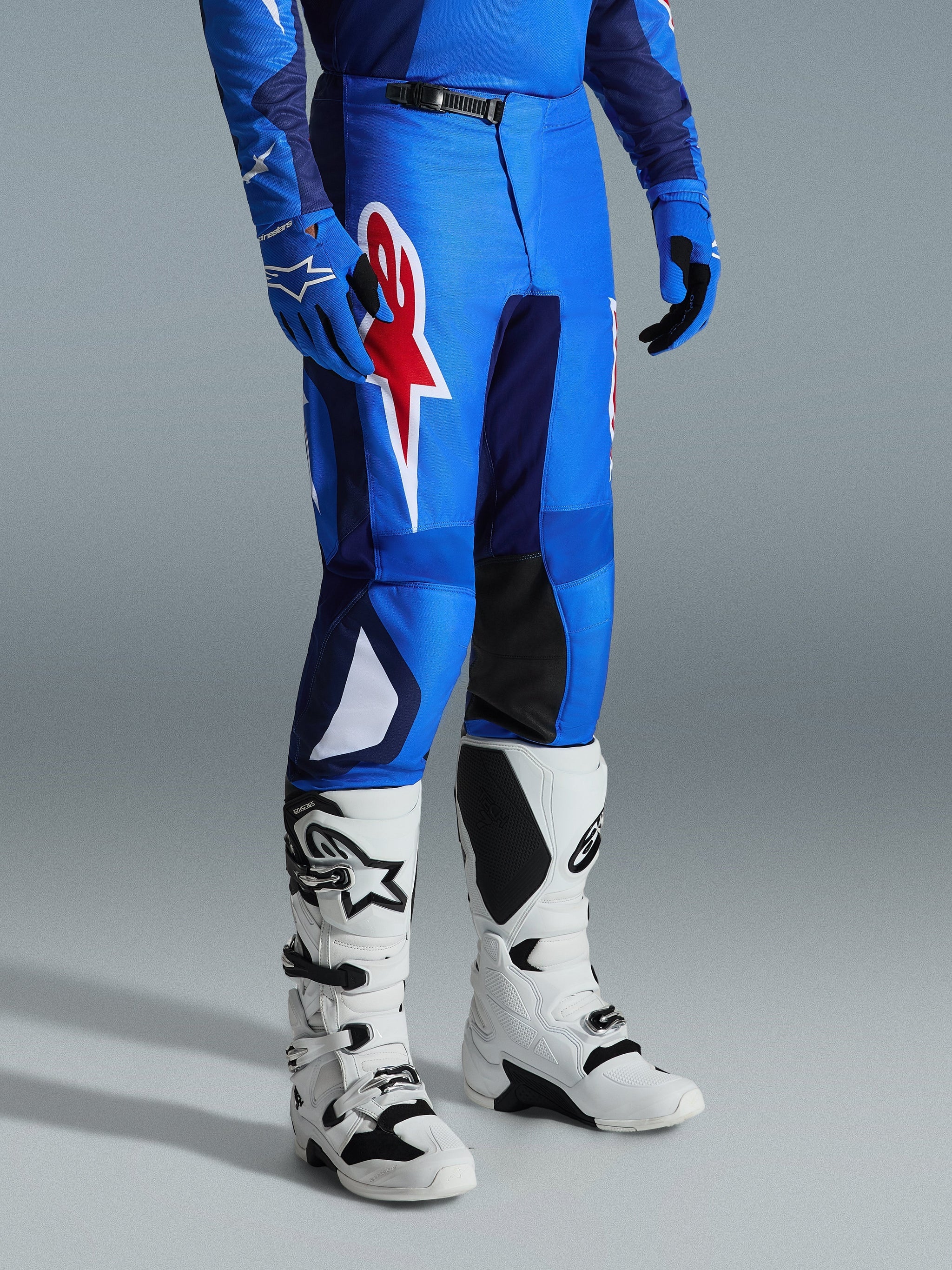 Alpinestars 2026 Fluid Grid Pants, pantalones de motocross, azul y rojo, usados con botas de motocross blancas y guantes azules, con un gran logotipo de estrella roja en el muslo y paneles internos negros en las rodillas, diseñados para conducción off-road