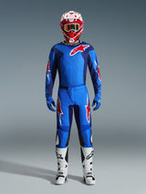 Piloto de motocross con pantalones Alpinestars 2026 Fluid Grid en azul y rojo, jersey azul a juego con el logotipo de Astars en rojo, casco rojo y blanco con gafas, guantes azules y botas de motocross blancas, equipamiento completo y coordinado para carreras todoterreno