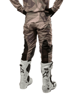Alpinestars 2024 Racer Tactical Pants, pantalones de motocross, camuflaje verde militar y marrón, vista trasera que muestra el patrón de camuflaje y paneles elásticos transpirables negros en la parte inferior de las piernas, usados con botas de motocross blancas, equipo técnico duradero para conducción todoterreno
