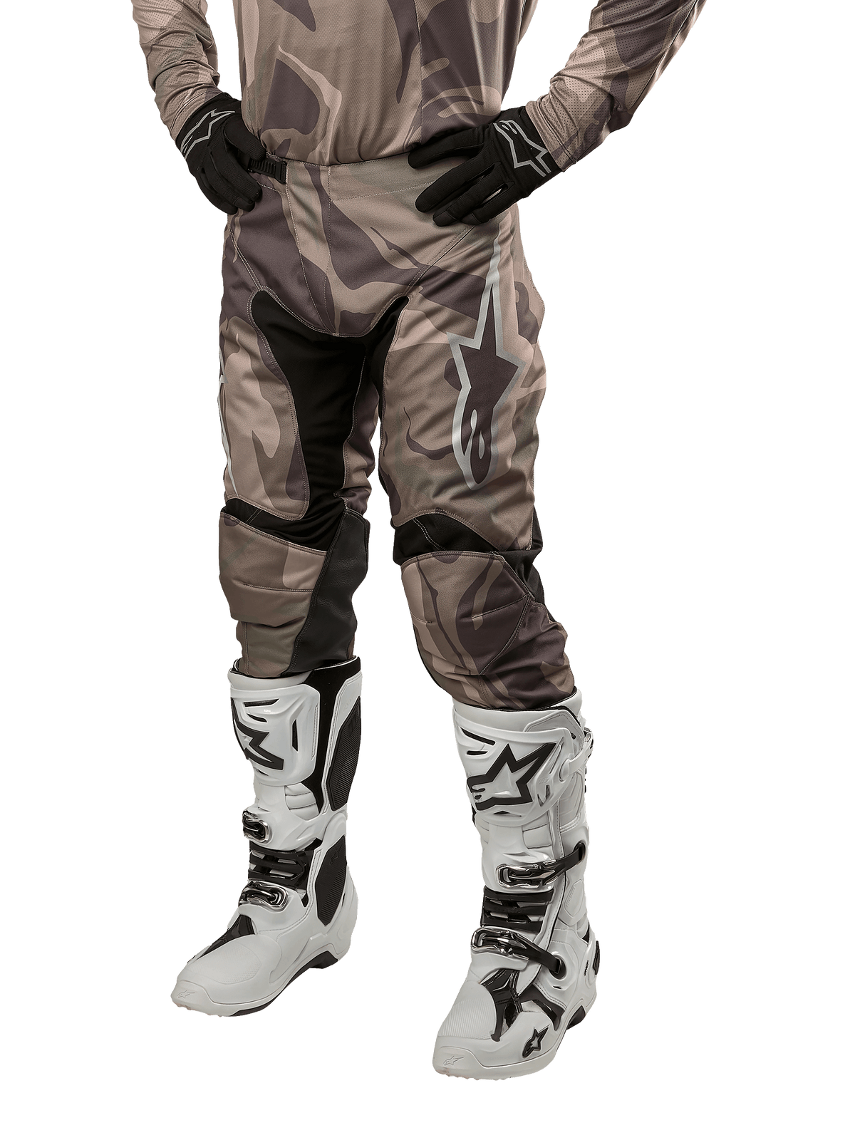 Alpinestars 2024 Racer Tactical Pants, pantalones de motocross en camuflaje verde militar y marrón, usados con jersey de camuflaje a juego, guantes negros y botas blancas con logos de estrella, con paneles elásticos negros y diseño ergonómico, equipo para todoterreno sobre fondo blanco.