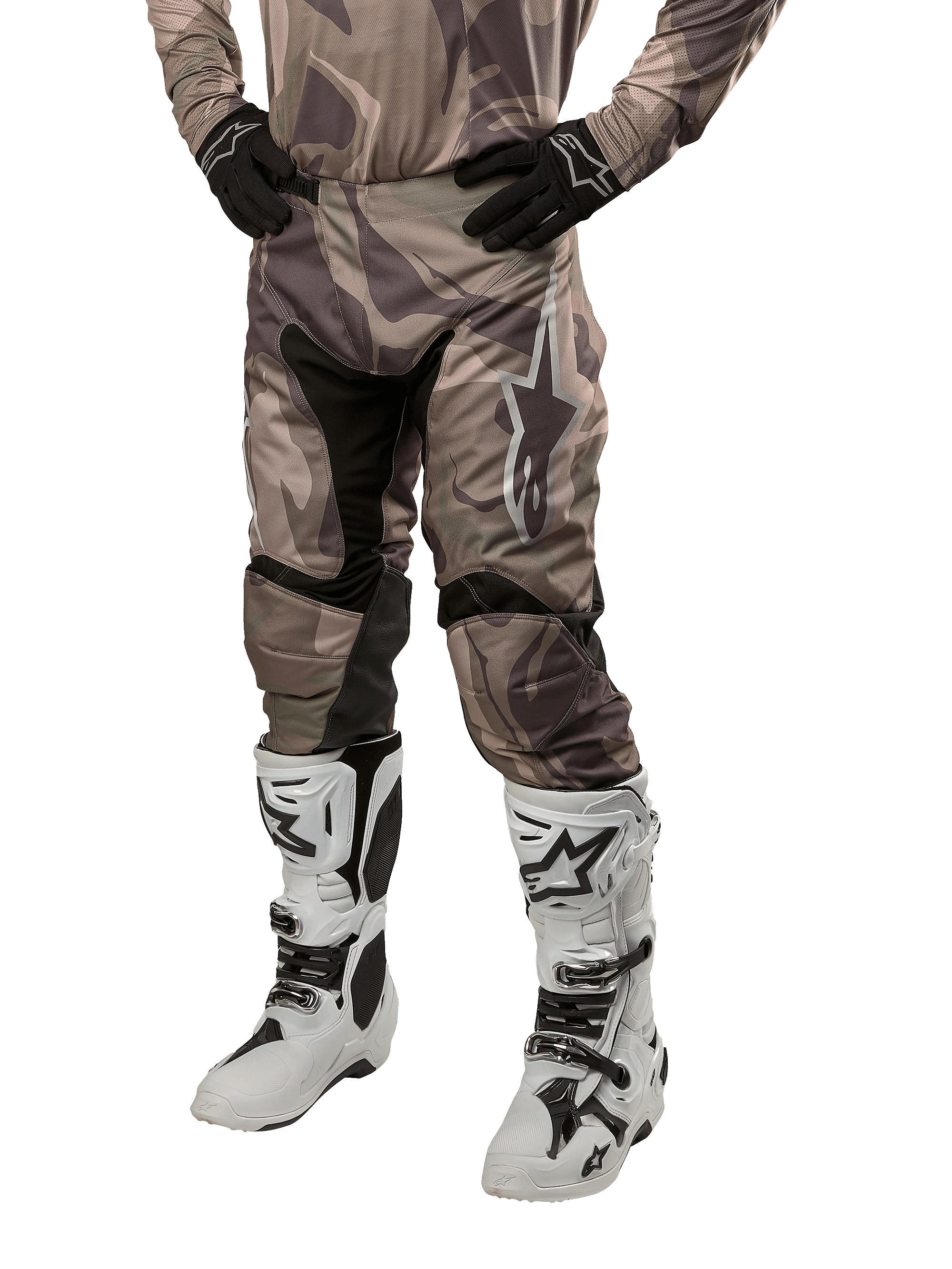 Alpinestars 2024 Racer Tactical Pants, pantalones de motocross en camuflaje verde militar y marrón, usados con jersey de camuflaje a juego, guantes negros y botas blancas con logos de estrella, con paneles elásticos negros y diseño ergonómico, equipo para todoterreno sobre fondo blanco.