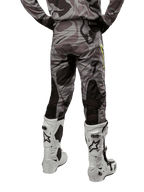Alpinestars 2024 Racer Tactical Pants, pantalones de motocross, color Cast Gray Camo Magnet, vista trasera que muestra el patrón de camuflaje y paneles elásticos negros transpirables, usados con botas de motocross blancas y negras, diseñados para competición off-road.