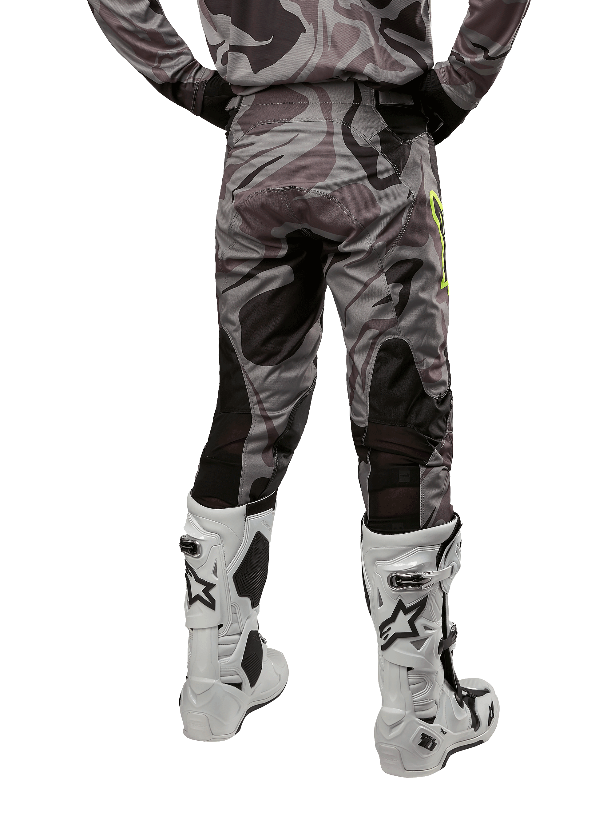 Alpinestars 2024 Racer Tactical Pants, pantalones de motocross, color Cast Gray Camo Magnet, vista trasera que muestra el patrón de camuflaje y paneles elásticos negros transpirables, usados con botas de motocross blancas y negras, diseñados para competición off-road.
