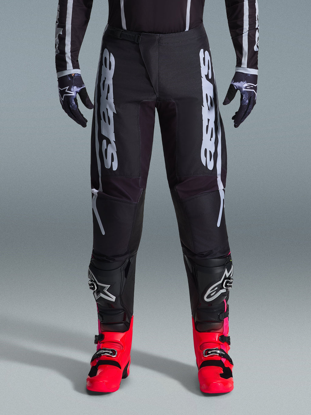 Alpinestars 2026 Fluid Apex Pants, pantalones de motocross negros con grandes letras blancas, combinados con rodilleras negras y botas rojas vibrantes, chasis ligero de polifabric 600D, diseño de ajuste deportivo para carreras off-road