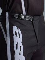 Alpinestars 2026 Fluid Apex Pants, pantalones de motocross, negro y gris, detalle en primer plano del sistema de cierre de trinquete integrado para un ajuste seguro, con gráficos del logotipo en blanco sobre polifabric 600D duradero