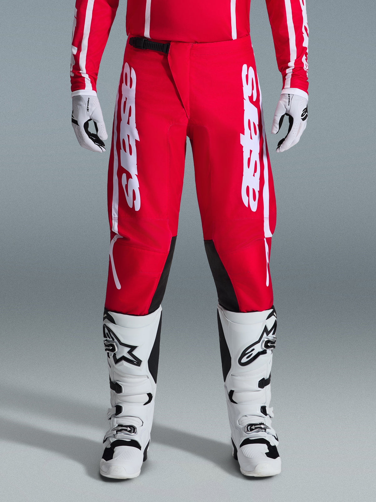 Pantalones Alpinestars 2026 Fluid Apex, pantalones de motocross, rojos y blancos, con grandes logotipos Astars blancos en los muslos y paneles interiores negros en las rodillas, combinados con botas y guantes blancos y negros para un look completo de carreras off-road.