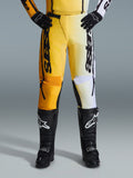 Alpinestars 2026 Fluid Apex Pants, pantalones de motocross, amarillos y negros, diseño de colores divididos con paneles amarillos y blancos, marca vertical 'astars' llamativa, usados con botas y guantes de motocross negros, equipamiento de alto rendimiento para conducción off-road