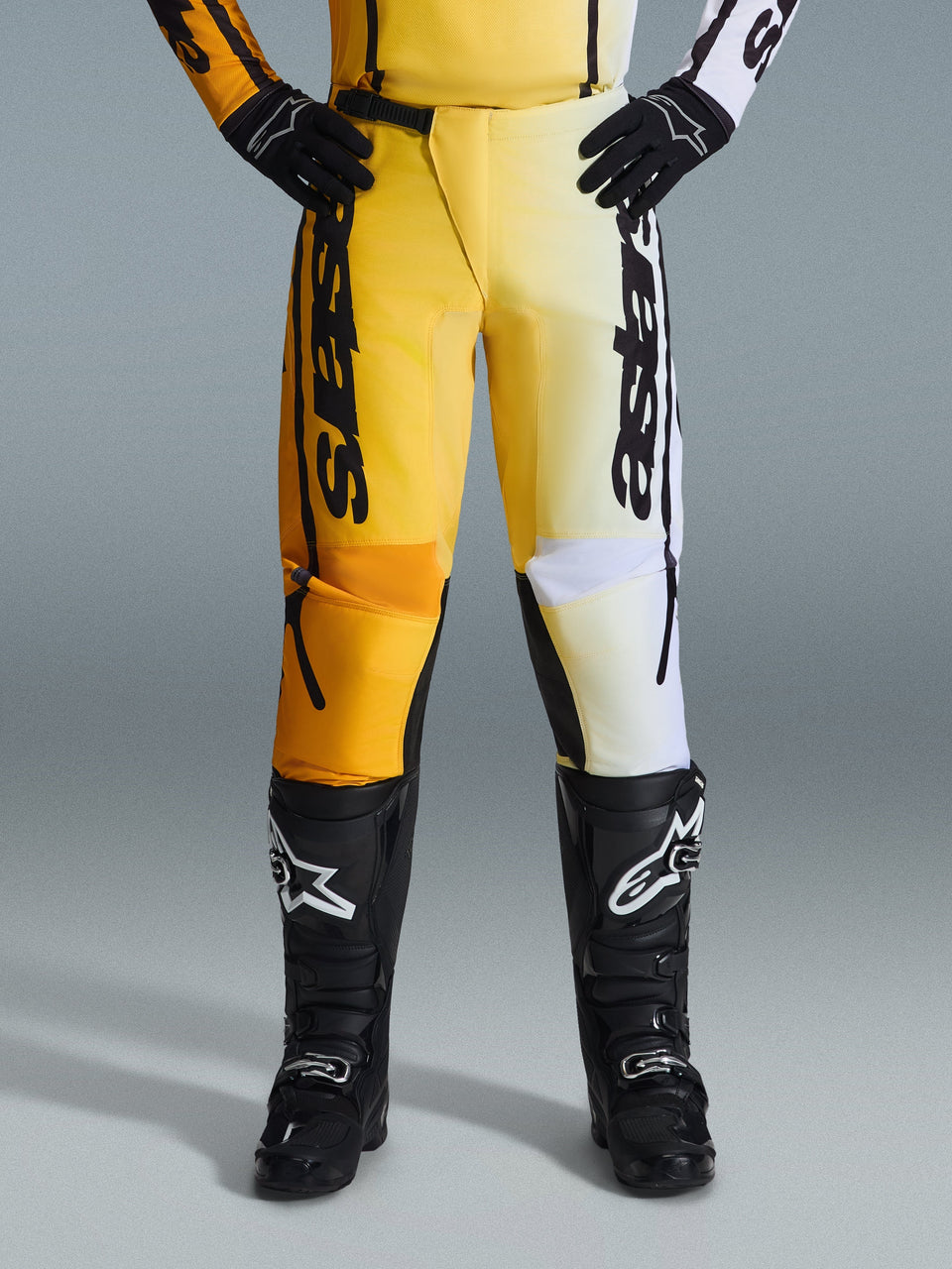 Alpinestars 2026 Fluid Apex Pants, Motocross Pants, Yellow and Black, split-color design with yellow and white panels, bold vertical 'astars' branding, worn with black motocross boots and gloves, performance gear for off-road riding