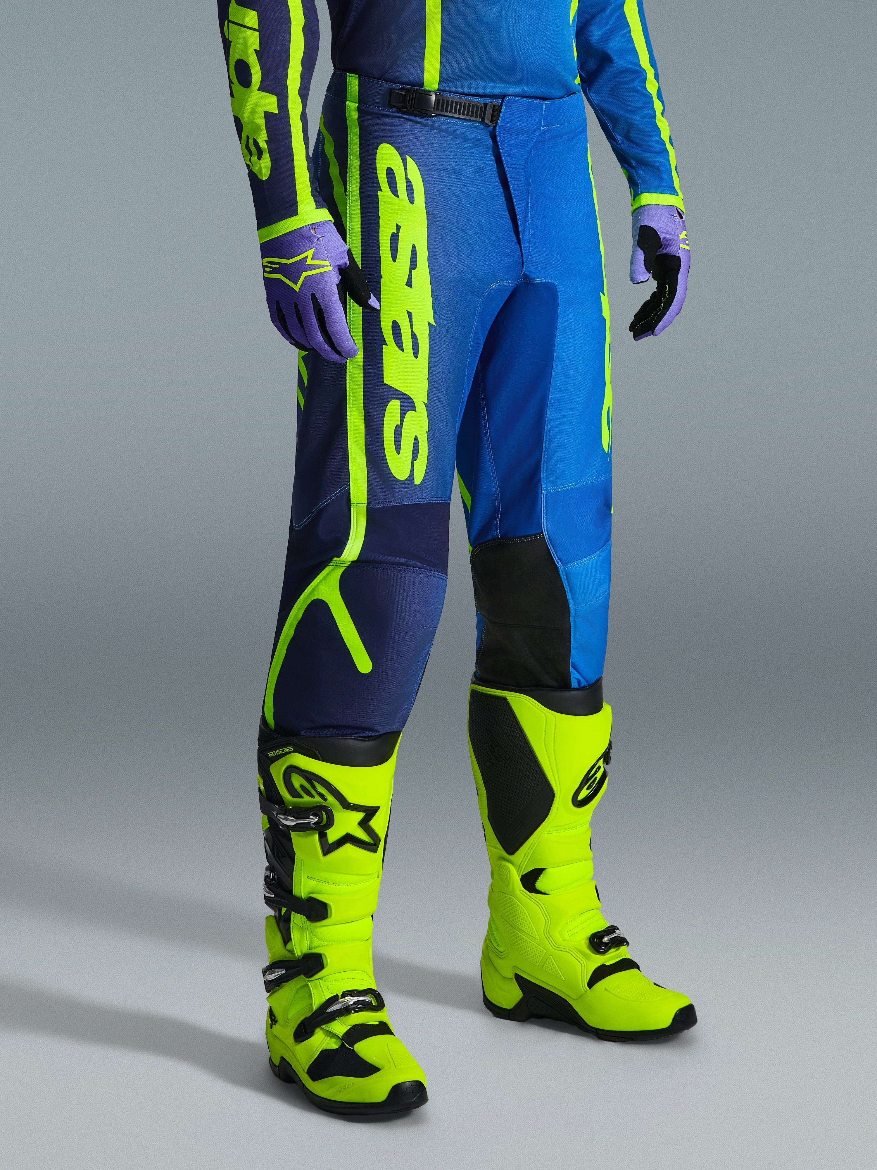 Alpinestars 2026 Fluid Apex Pants, pantalones de motocross, azul y amarillo flúor, combinados con guantes a juego y botas de color amarillo flúor brillante, con logotipos verticales llamativos, paneles reforzados en las rodillas y un cierre de cintura de trinquete seguro.