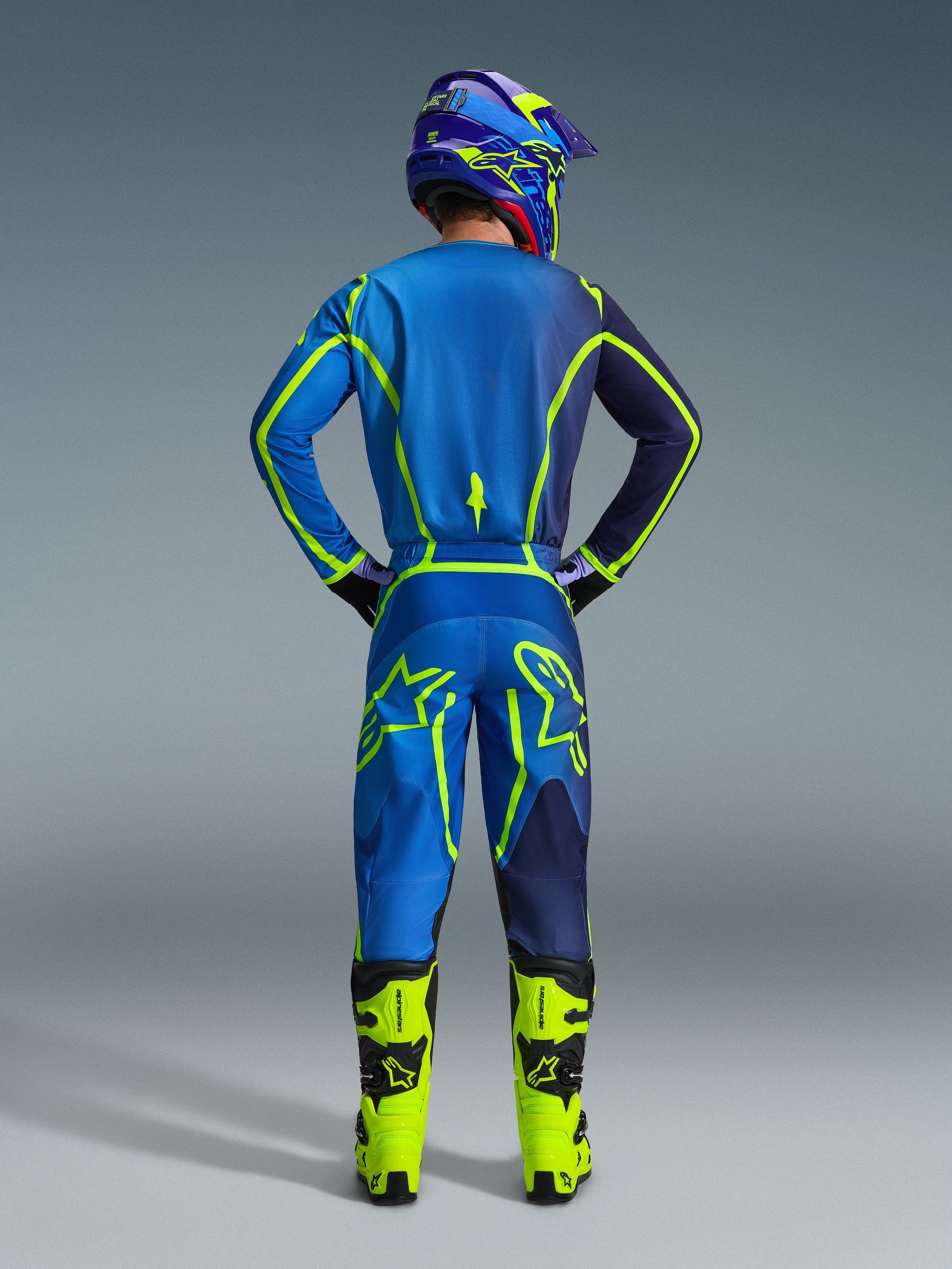 Pantalones Alpinestars 2026 Fluid Apex, pantalones de motocross, azul y amarillo flúor, vista trasera del piloto con equipo de carreras completo, jersey y casco a juego, botas amarillo brillante, ajuste atlético coordinado para motocross.