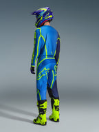 Piloto de motocross visto desde atrás con pantalones Alpinestars Fluid Apex 2026 en azul y amarillo flúor, jersey y casco a juego en azul y amarillo, y botas amarillo neón brillante, equipo de competición coordinado para rendimiento off-road
