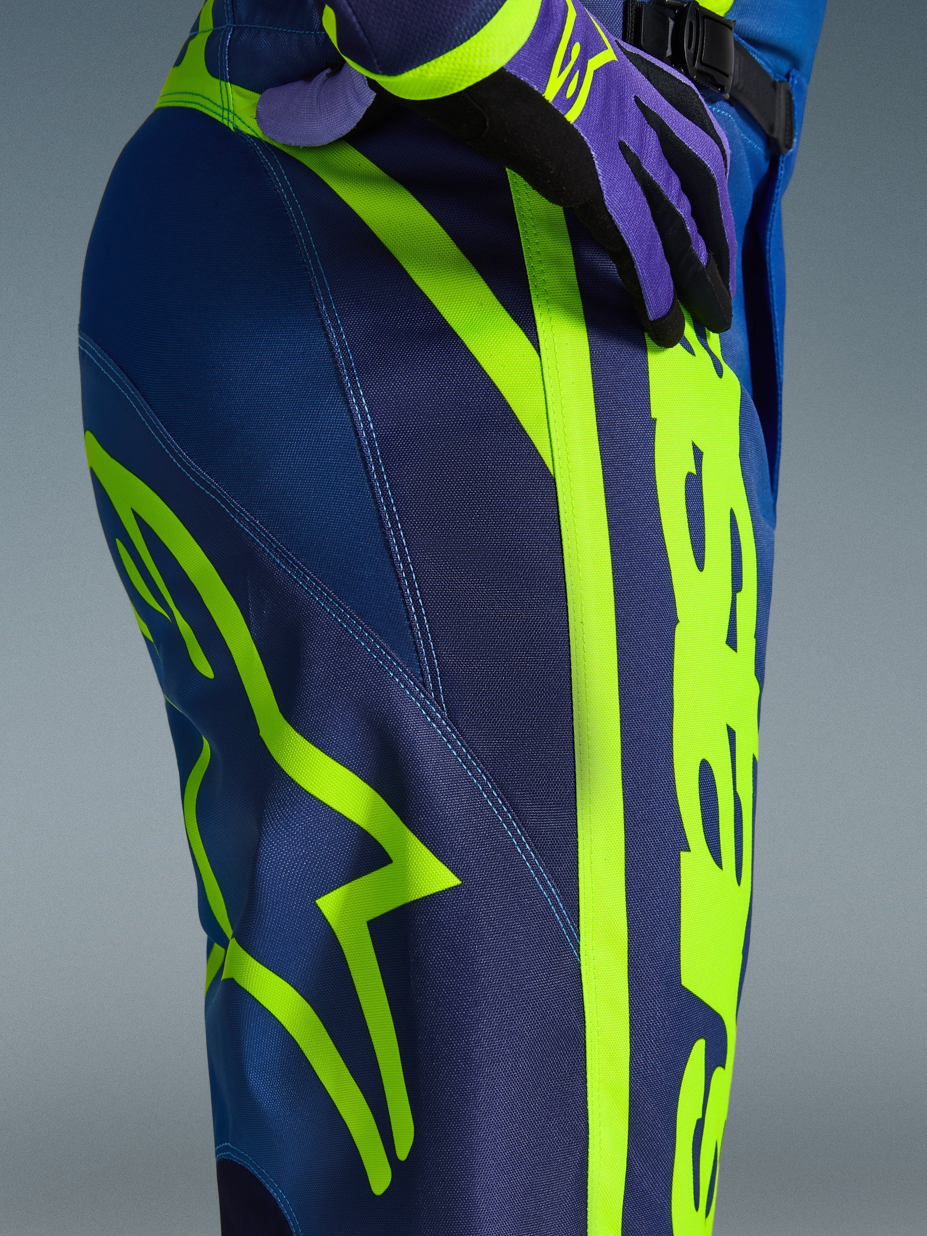 Alpinestars 2026 Fluid Apex Pants, pantalones de motocross, azul y amarillo flúor, primer plano del lateral y la cadera con el logotipo de Alpinestars en amarillo neón, material de polifabric duradero para conducción off-road, parte de un conjunto de equipamiento a juego