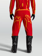 Pantalones Alpinestars Fluid Apex V2 de motocross para hombre, rojos y dorados, vista trasera con botas negras.
