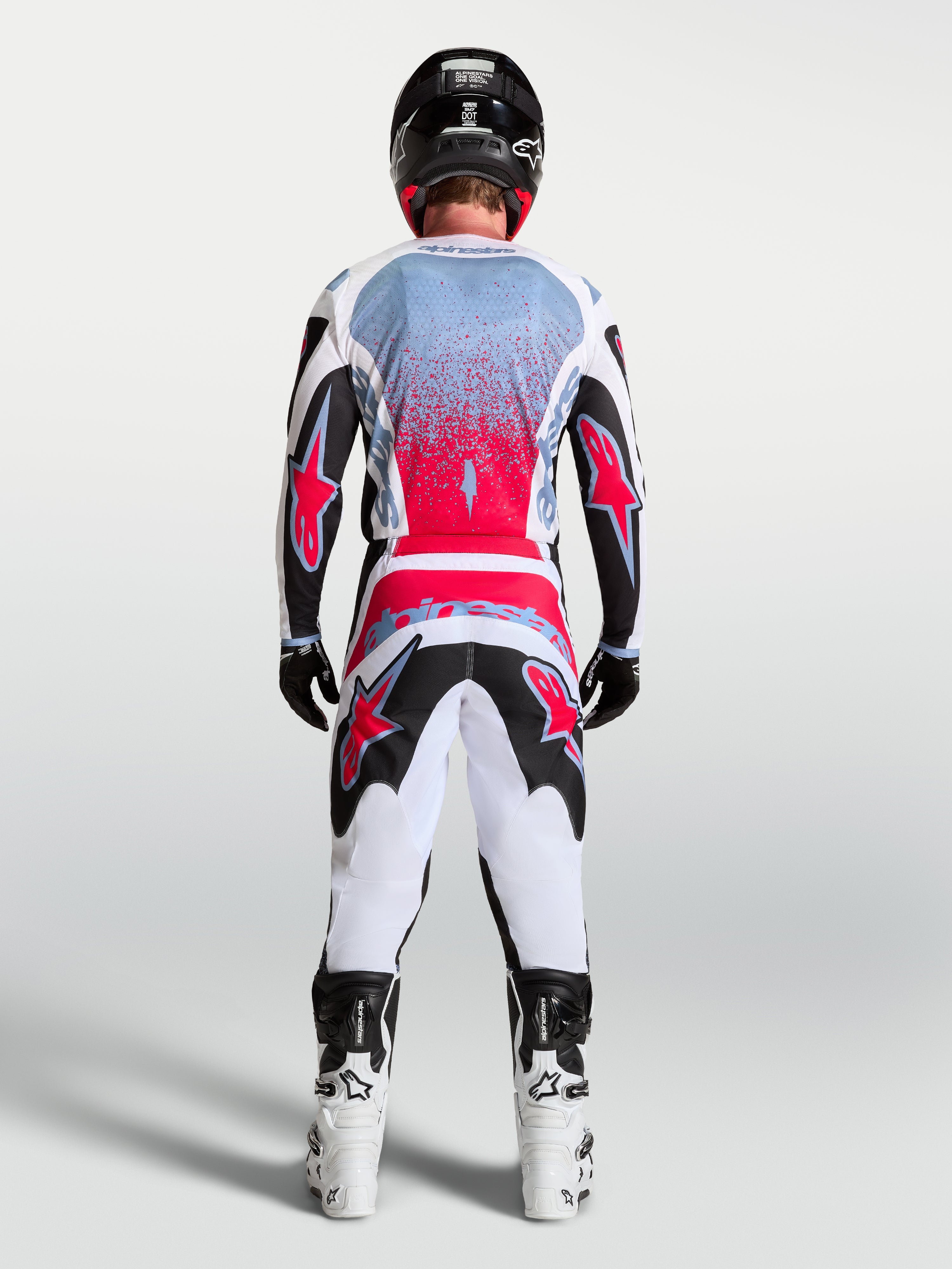 Alpinestars Pantalones Fluid Drag, pantalones de motocross para hombre, negros, blancos y rojo flúor, vista trasera de piloto con equipo completo, patrón 3D ergonómico