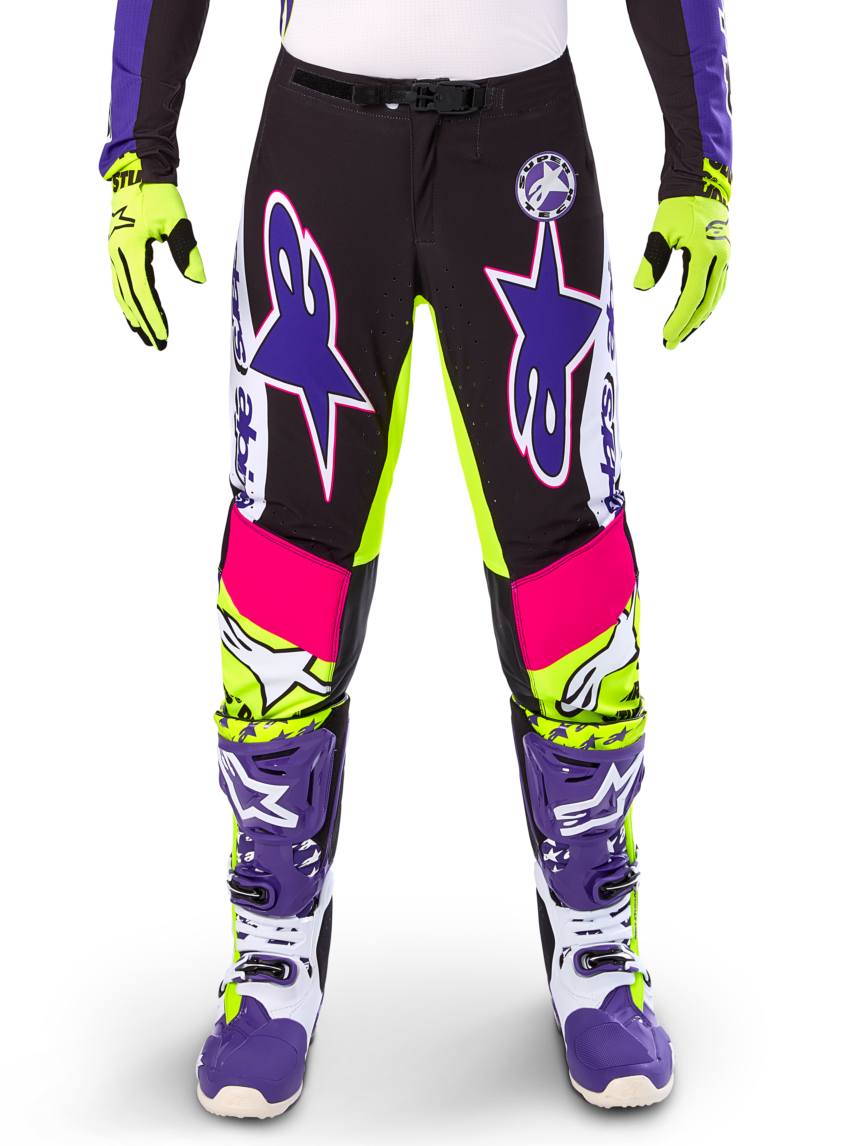 Pantalones Alpinestars Limited Edition Supertech Dirt Studios, pantalones de motocross, blanco, morado y amarillo flúor, con paneles negros y detalles en amarillo neón y rosa, grandes logotipos de estrellas moradas, mostrados con guantes amarillo neón y botas de carreras moradas, equipamiento duradero para carreras todoterreno
