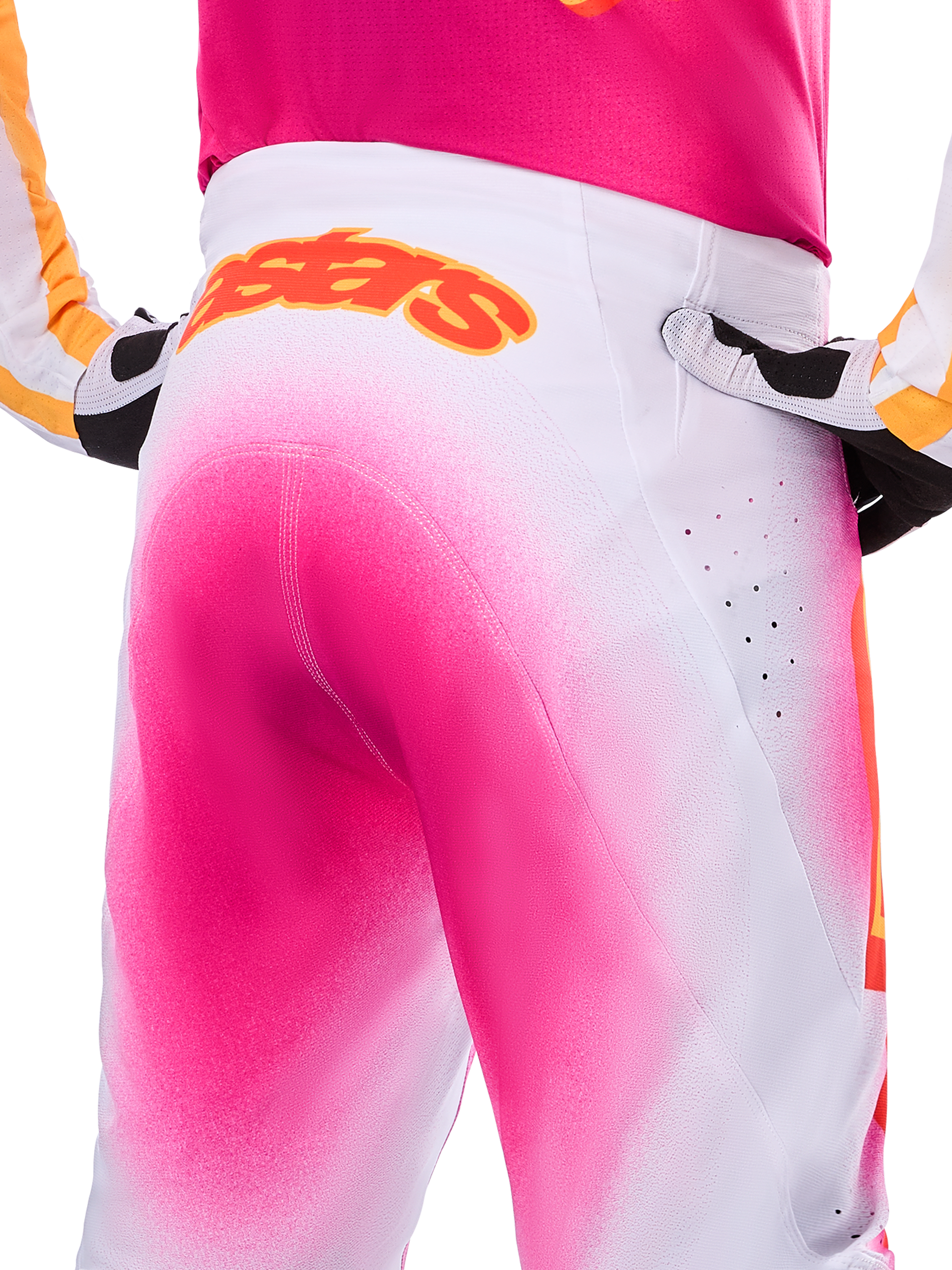 Alpinestars Limited Edition Supertech AFD MIG Pants, pantalones de motocross, rosa flúor y blanco con un efecto de degradado tipo pintura en aerosol, logotipo naranja grande de Alpinestars en la parte posterior de la cintura, vista de primer plano que muestra el ajuste atlético y las perforaciones de ventilación.