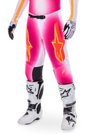 Alpinestars Supertech AFD MIG Limited Edition, pantalones de motocross rosas con logotipos de estrellas en naranja y amarillo, usados con botas de motocross blancas y guantes blancos y negros, con paneles internos negros en las rodillas y un ajuste atlético, parte de un conjunto de equipamiento de alto rendimiento