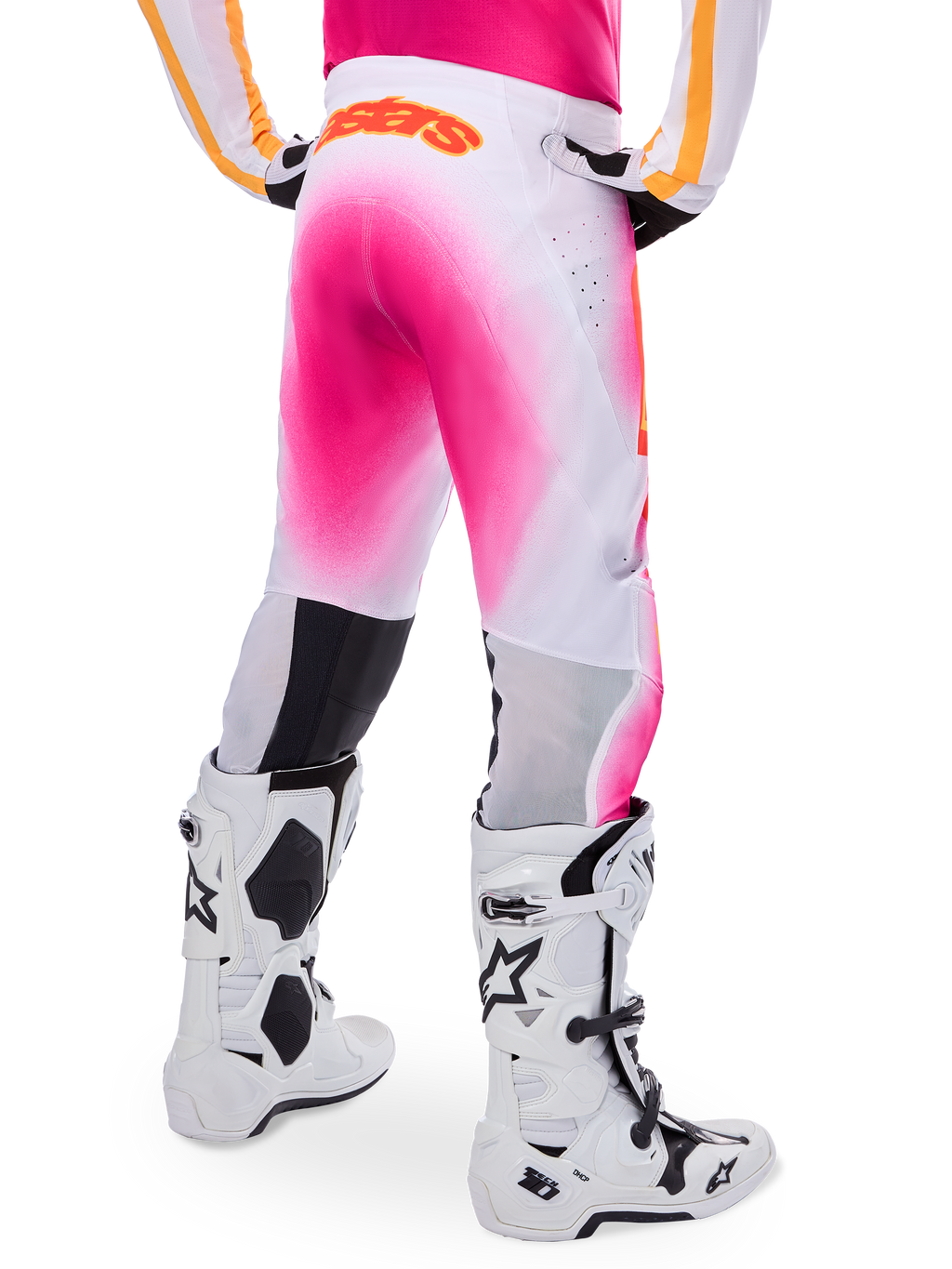 Pantalones de motocross Alpinestars Supertech AFD MIG Edición Limitada, en rosa y blanco, vista trasera con un vibrante efecto de degradado rosa, logotipo naranja en la cintura posterior, combinados con botas Tech 10 blancas y negras, equipamiento profesional para carreras todoterreno