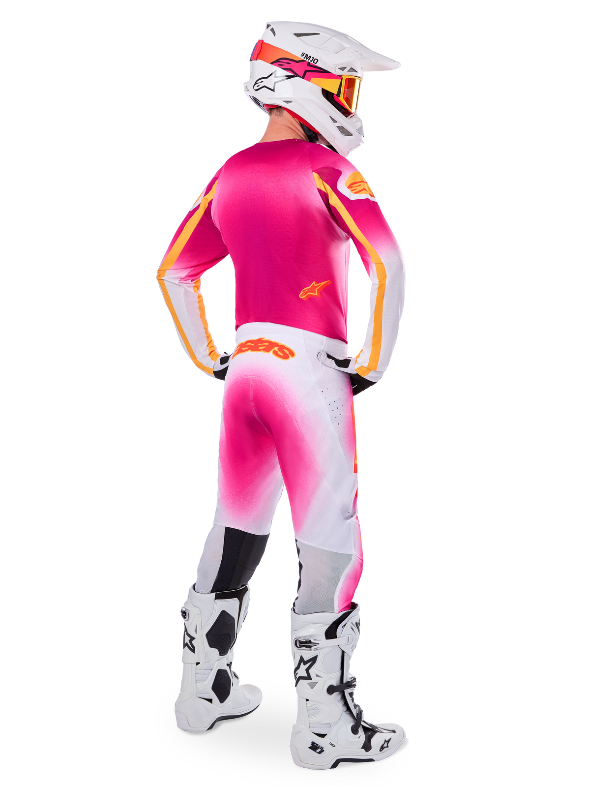 Piloto de motocross visto desde atrás con el conjunto de equipamiento de edición limitada Supertech AFD MIG, jersey rosa con detalles naranjas, pantalones blancos con degradado rosa y marca Alpinestars naranja, casco blanco con gráficos rosas y gafas naranjas, botas blancas y negras, kit de competición profesional para todoterreno
