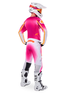 Piloto de motocross visto desde atrás con el conjunto de equipamiento de edición limitada Supertech AFD MIG, jersey rosa con detalles naranjas, pantalones blancos con degradado rosa y marca Alpinestars naranja, casco blanco con gráficos rosas y gafas naranjas, botas blancas y negras, kit de competición profesional para todoterreno