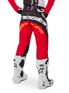 Alpinestars Techstar Deep Pants Edición Limitada, pantalones de motocross en negro, blanco y rojo intenso, vista posterior con un llamativo logo de Alpinestars en blanco sobre el asiento y detalles en naranja, usados con botas técnicas blancas para competición profesional de motocross