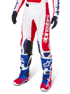 Alpinestars Techstar Fortitude Edición Limitada, pantalones de motocross en rojo brillante, blanco y azul, usados con botas y guantes de off-road a juego, con marca vertical en la pierna, paneles perforados transpirables y secciones de rodilla reforzadas en negro, diseño de ajuste atlético de carrera