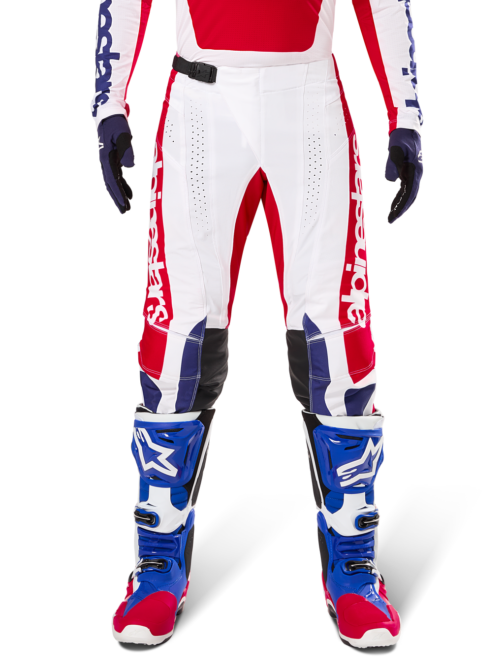 Alpinestars Limited Edition Techstar Fortitude Pants, pantalones de motocross en rojo brillante, blanco y azul, usados con equipamiento a juego que incluye botas protectoras y guantes azules, con chasis blanco y gráficos rojos, paneles de cuero negro en las rodillas y perforaciones cortadas con láser, ropa de competición profesional todoterreno