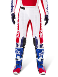Alpinestars Limited Edition Techstar Fortitude Pants, pantalones de motocross en rojo brillante, blanco y azul, usados con equipamiento a juego que incluye botas protectoras y guantes azules, con chasis blanco y gráficos rojos, paneles de cuero negro en las rodillas y perforaciones cortadas con láser, ropa de competición profesional todoterreno
