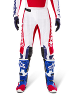 Alpinestars Limited Edition Techstar Fortitude Pants, pantalones de motocross en rojo brillante, blanco y azul, usados con equipamiento a juego que incluye botas protectoras y guantes azules, con chasis blanco y gráficos rojos, paneles de cuero negro en las rodillas y perforaciones cortadas con láser, ropa de competición profesional todoterreno