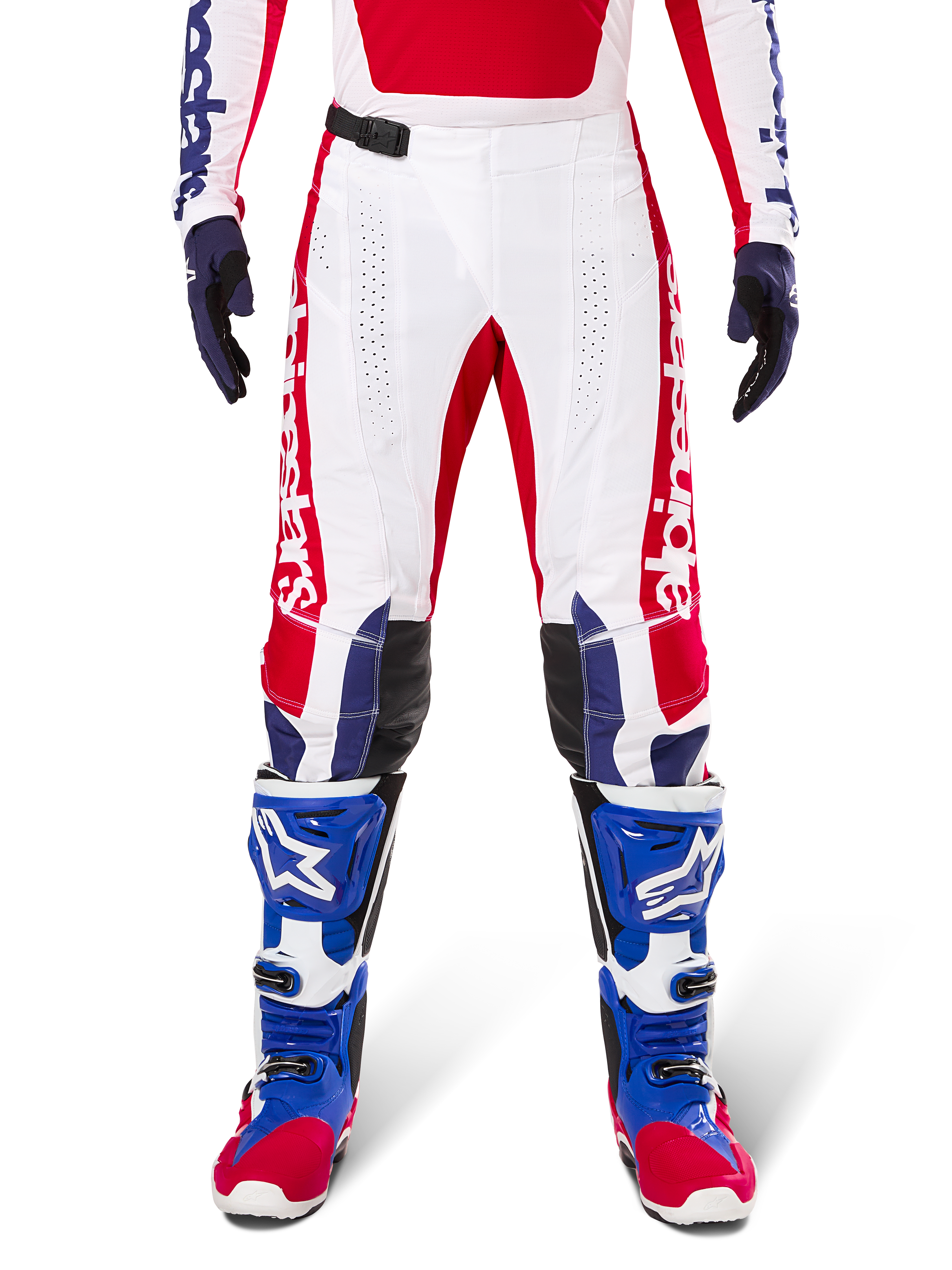 Alpinestars Limited Edition Techstar Fortitude Pants, pantalones de motocross en rojo brillante, blanco y azul, usados con equipamiento a juego que incluye botas protectoras y guantes azules, con chasis blanco y gráficos rojos, paneles de cuero negro en las rodillas y perforaciones cortadas con láser, ropa de competición profesional todoterreno