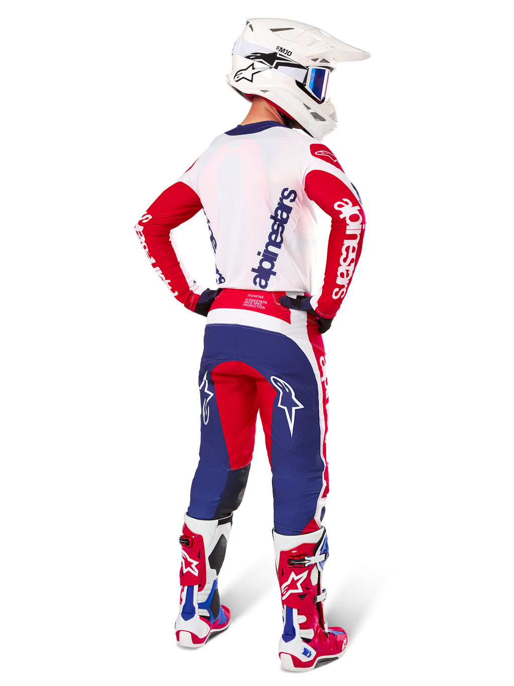 Pantalones Alpinestars Techstar Fortitude Edición Limitada, pantalones de motocross, rojo brillante, blanco y azul, mostrados en un piloto desde atrás con camiseta, botas y casco a juego, resaltando el ajuste atlético y la llamativa ubicación de los logotipos.