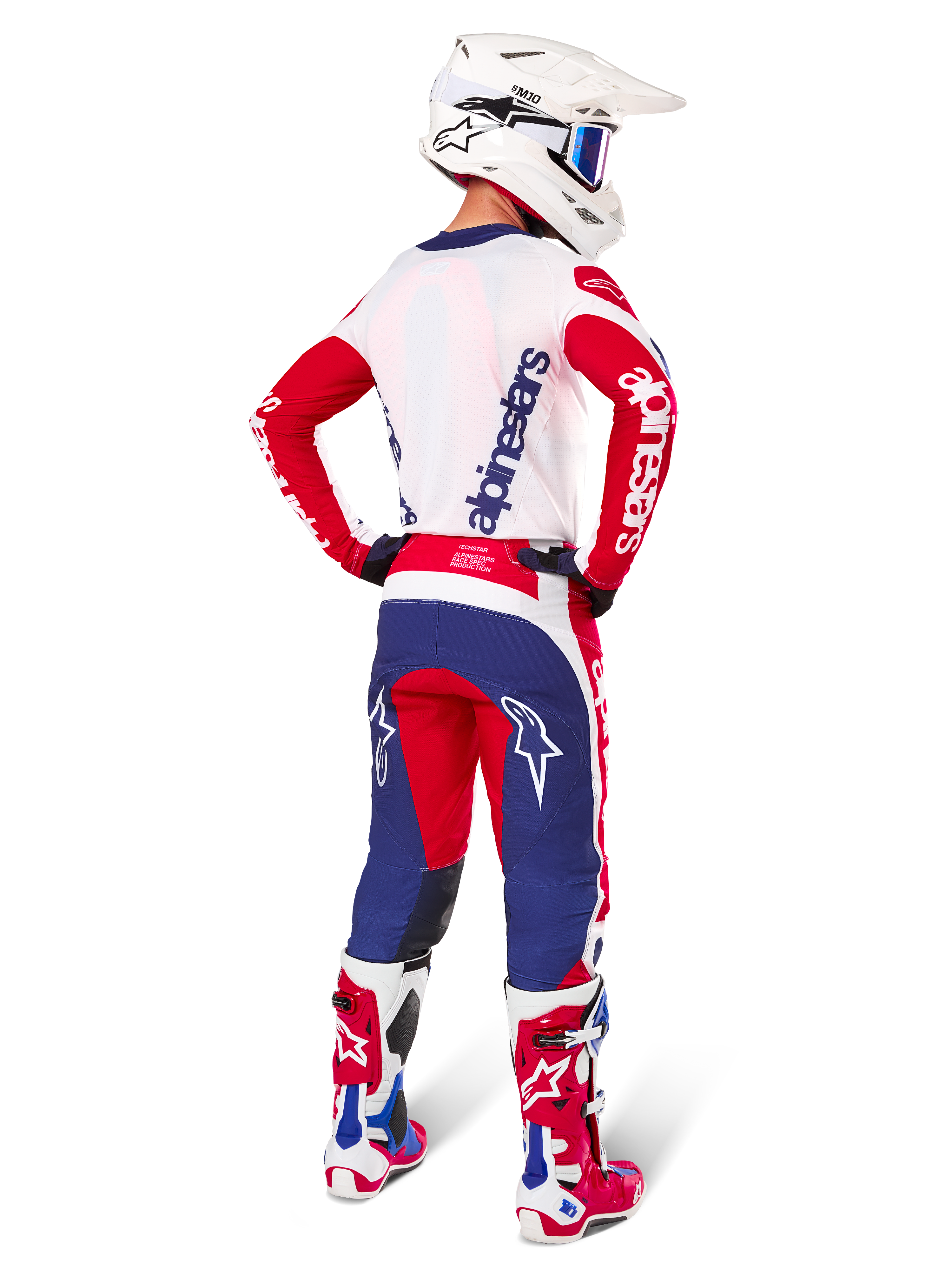 Pantalones Alpinestars Techstar Fortitude Edición Limitada, pantalones de motocross, rojo brillante, blanco y azul, mostrados en un piloto desde atrás con camiseta, botas y casco a juego, resaltando el ajuste atlético y la llamativa ubicación de los logotipos.