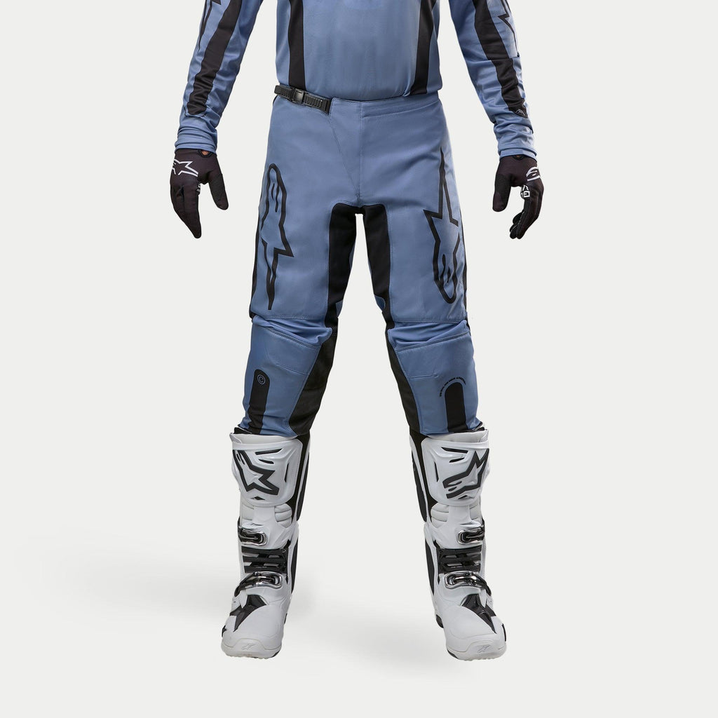 Pantalones Alpinestars Fluid Lurv 2024, pantalones de motocross, azul claro y negro, usados con botas de carreras blancas y negras y guantes a juego, con logotipos de estrellas negras en los muslos y diseño ergonómico para rendimiento todoterreno