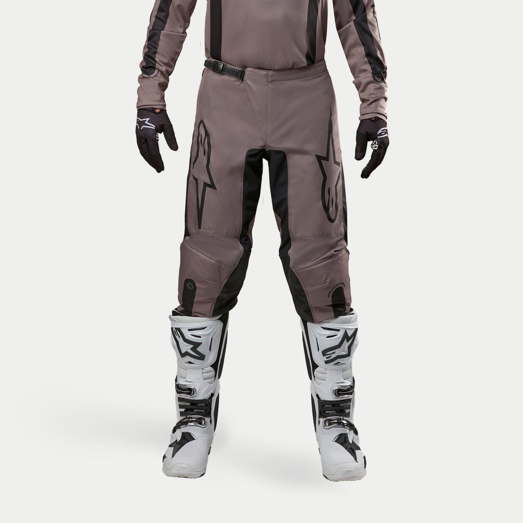 Pantalones Alpinestars Fluid Lurv 2024, pantalones de motocross, Mud Black, usados con jersey a juego, guantes negros y botas blancas, con logotipos negros grandes en los muslos, ajuste ergonómico y material duradero para carreras fuera de carretera
