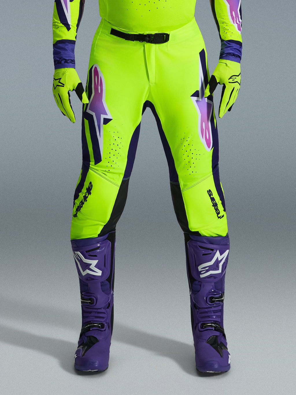 Pantalones Alpinestars Supertech Vista 2026, pantalones de motocross, amarillo fluorescente, morado y negro, usados con guantes a juego y botas moradas, con logotipos grandes degradados en los muslos, zonas perforadas para ventilación y un diseño atlético profesional para carreras todoterreno